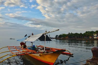 Outrigger boat moored in sea against cloudy sky