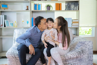 Asian beautiful young parents are kissing their cute little daughter, who is looking at camera