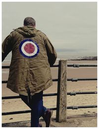 Rear view of man standing at beach against sky