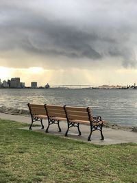 Empty bench by sea against sky during sunset