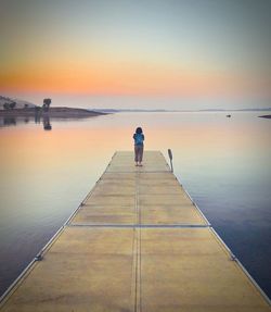 Rear view of woman standing on jetty at sunset