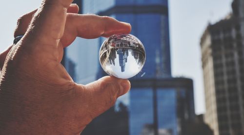 Close-up of hand holding crystal ball against skyline