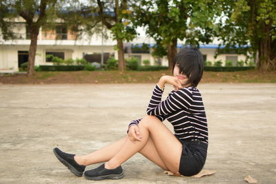 Side view of young woman with short hair sitting on footpath