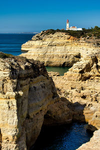 Lighthouse on rocks by sea against sky