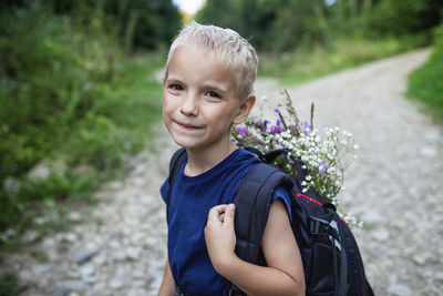 Little hiker with backpack comes from the mountain and carries a bouquet of wildflowers