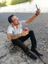 Mid adult man taking selfie with mobile phone while sitting on road