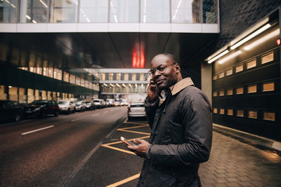 Portrait of businessman with smart phone listening music while standing on road against building in city