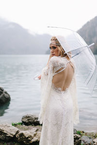 A beautiful young woman bride in a wedding lace dress stands in the middle of a lake and mountains