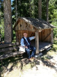 Full length portrait of man sitting at hut in forest