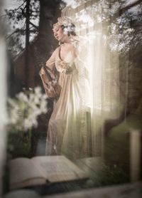 Woman standing by cross against trees in forest