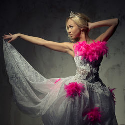 Beautiful young woman in pink and white wedding dress dancing against wall