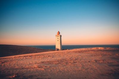 Lighthouse on beach by sea against clear sky