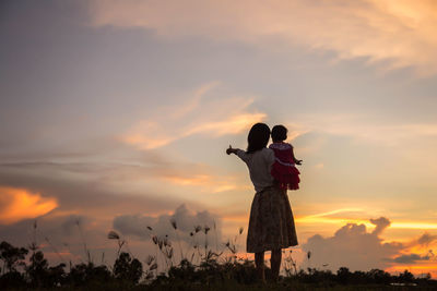 Rear view of woman standing against sky during sunset