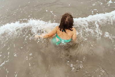 Rear view of boy splashing water in sea