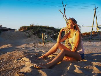 Young woman sitting on swing at beach against clear sky