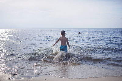 Happy sibling running into the sea and splashing in sunset light, lots of fun and happiness, summer 