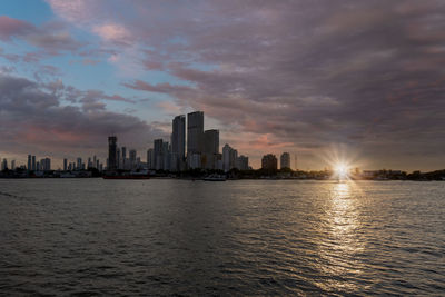 Sea by buildings against sky during sunset