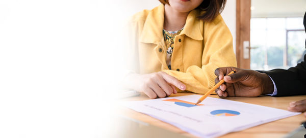 Midsection of woman reading book while sitting on table