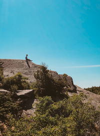 Teen boy sitting on top of a rocky hill on a hike on a sunny day.