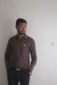 Portrait of young man wearing sunglasses standing against wall