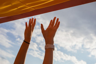 Low angle view of cropped hands against sky