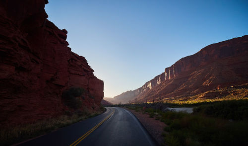 Road leading towards mountains against clear sky
