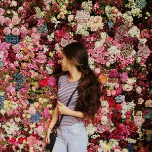 Young woman standing against various flowers