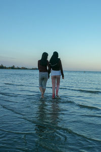 Rear view of women standing at beach against clear sky during sunset