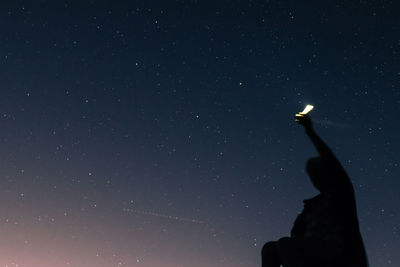 Low angle view of silhouette man holding illuminated flashlight against star field