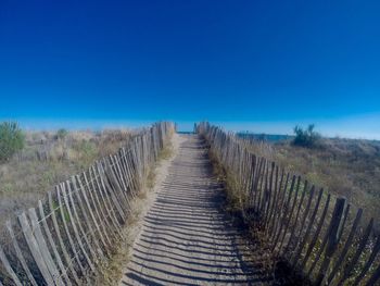 Boardwalk on field against clear blue sky