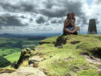 Portrait of happy man and woman on hill against cloudy sky