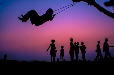 Silhouette children on playground against clear sky during sunset