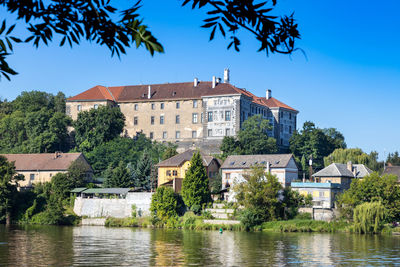 Buildings by river against blue sky