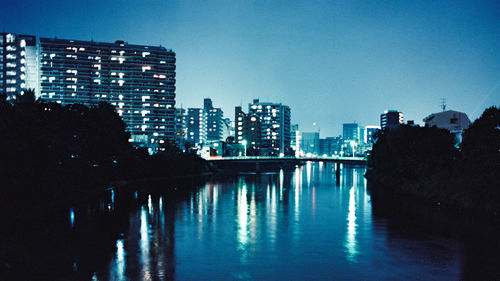 Illuminated city by river against clear sky at night