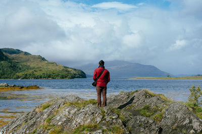 Rear view of man standing on rock by sea against sky