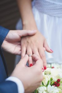 Cropped image of bridegroom putting ring in hand of bride