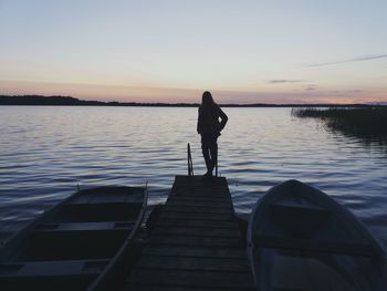 Silhouette woman standing on pier over lake against sky during sunset