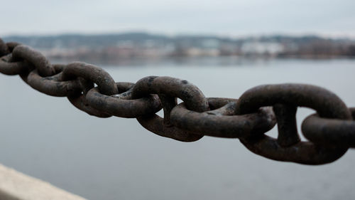 Close-up of rusty chain against river