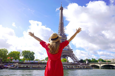 Woman traveler with hat and arms raised on the seine river in paris. 