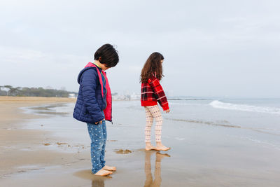 Side view of two girls playing at the beach watching sea waves