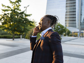 Black businessman standing in downtown and speaking on mobile phone while discussing work issues and looking away