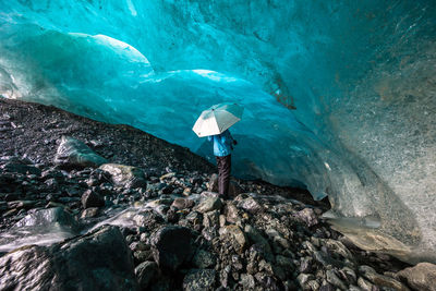 Person holding umbrella and standing in ice cave