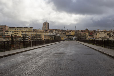 Empty road by buildings against sky in city