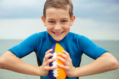 Portrait of happy playful boy holding rugby ball in sea