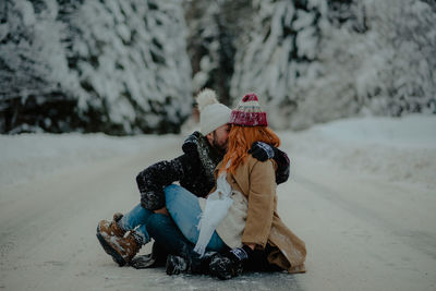 Full length of couple sitting on frozen road during winter