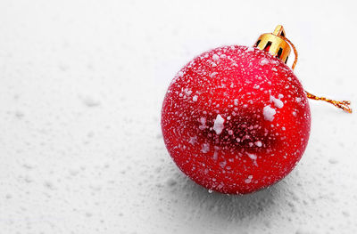 Close-up of red bauble with snow on white table
