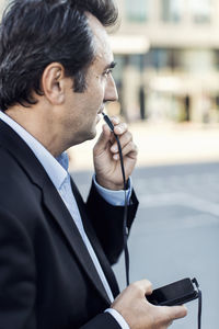 Side view of businessman communicating through headphones using mobile phone on street