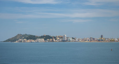 Sea by buildings in city against sky