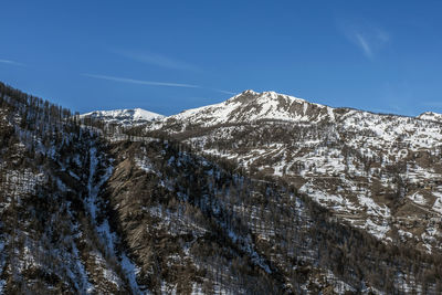 Low angle view of snowcapped mountains against blue sky