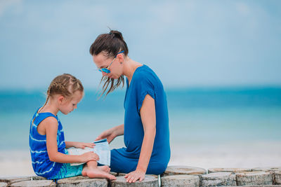 Side view of mother and daughter sitting at beach